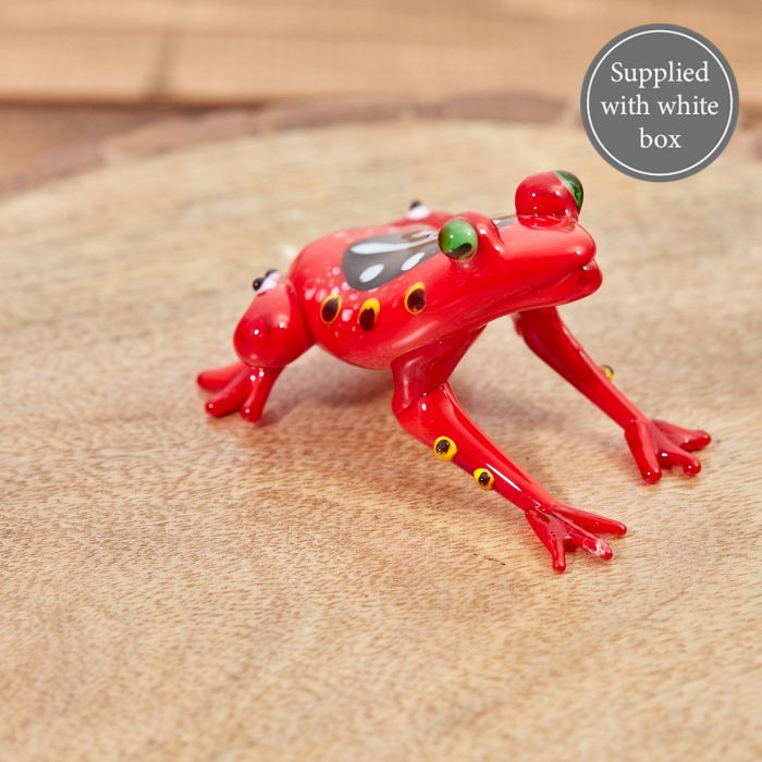 Bright red glass frog ornament with green eyes and black-and-yellow spotted details, displayed on a wooden surface. Supplied with white box.