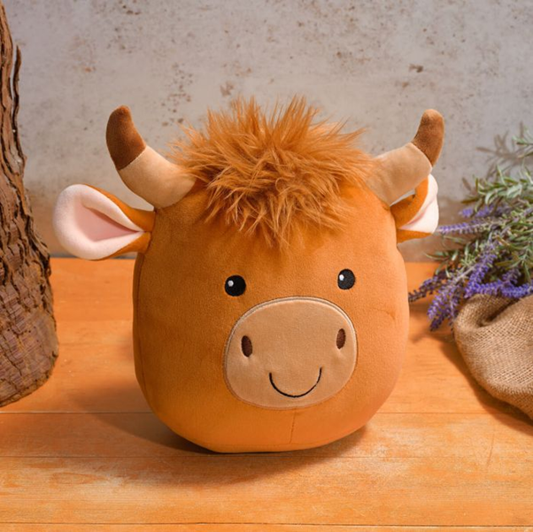 Cute soft toy Highland cow plush with fluffy hair and horns placed on a wooden table in a cosy home setting.